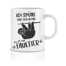 Lade das Bild in den Galerie-Viewer, Ein humorvolles Bild einer Tasse mit dem Schriftzug 'Ich spüre das Tier in mir, es ist ein Faultier.' und einem entspannten Faultier, das an einem Ast herunterhängt. Das Bild strahlt Entspannung und humorvolle Selbstreflexion aus